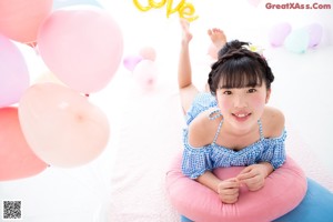 A young woman sitting on a pink rug holding a bunch of balloons.