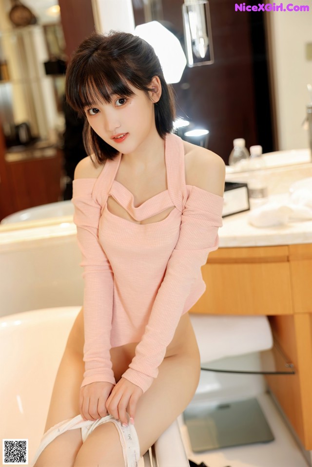 A woman in a pink sweater sitting in a bathtub.