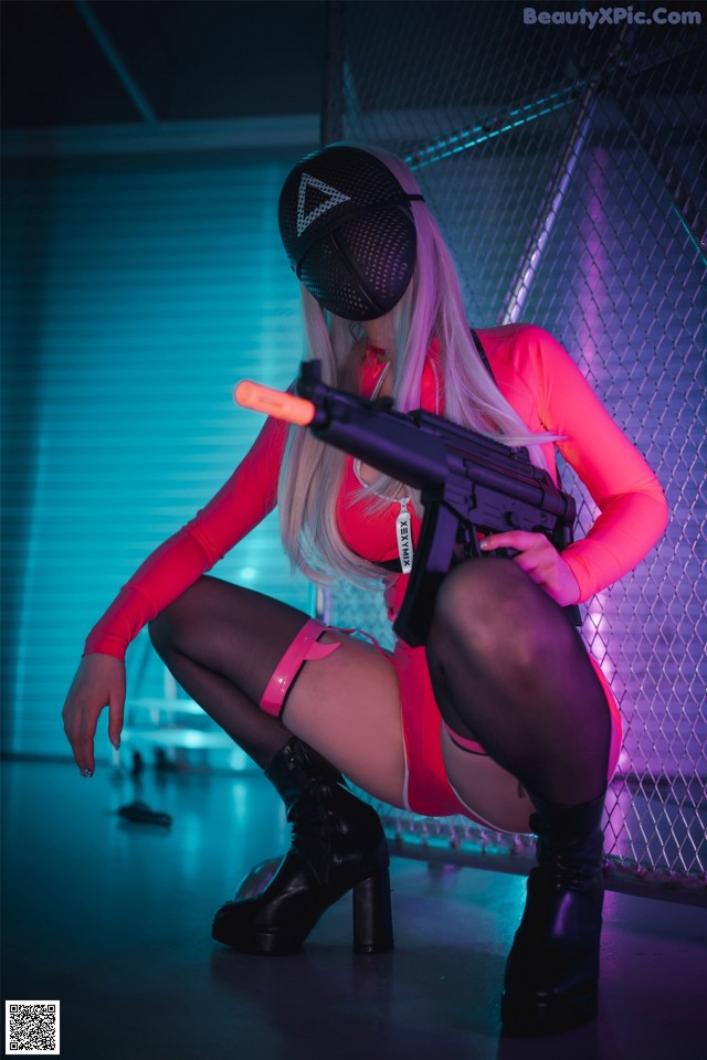 A woman in a pink outfit holding a gun.