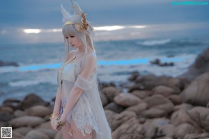 A woman in a white dress standing on a pier by the water.