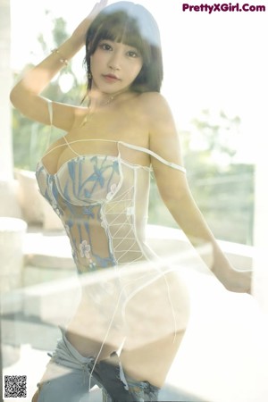 A woman in a white bodysuit standing in front of a window.