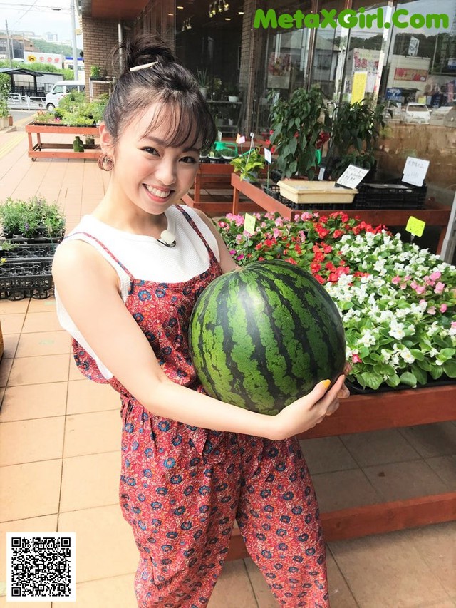 A woman holding a large watermelon in front of a store.