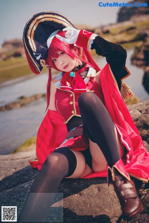 A woman in a red and black outfit sitting on a rock.