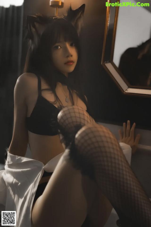 A woman in a black bra top and fishnet stockings sitting on a chair.