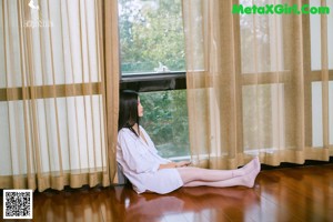 A woman sitting on the floor in a white shirt and stockings.