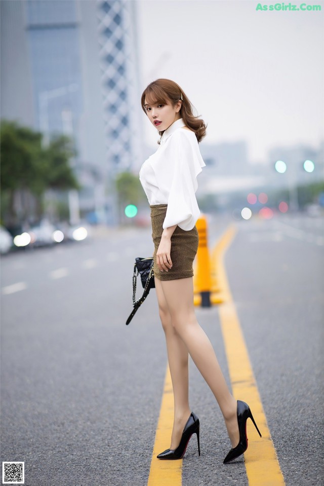 A woman in a white shirt and brown skirt is walking down the street.