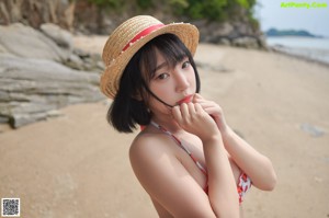 A woman in a bikini and hat on a beach.