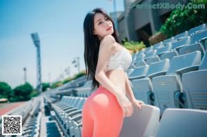 A woman in a white top and red pants sitting on a bench.