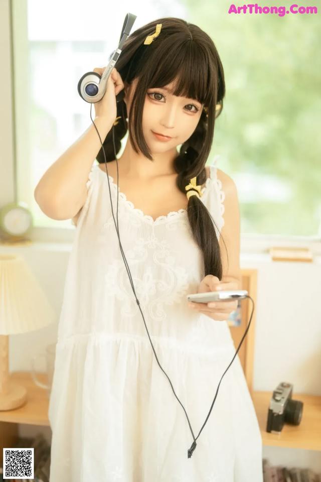 A woman in a white dress holding a cell phone and headphones.