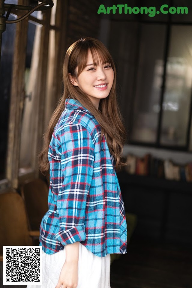A woman wearing a blue and red plaid shirt and white skirt.