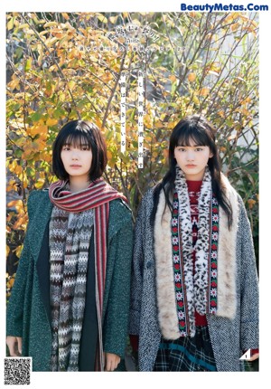 Two young women standing next to each other in front of tall grass.