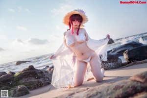 A woman with pink hair and a straw hat sitting on a beach.