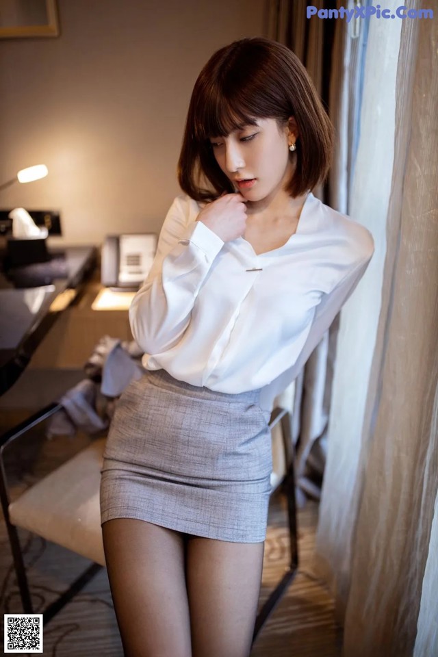 A woman in a white shirt and gray skirt posing for a picture.