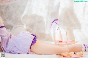 A woman in a pink and purple dress sitting on a bed.