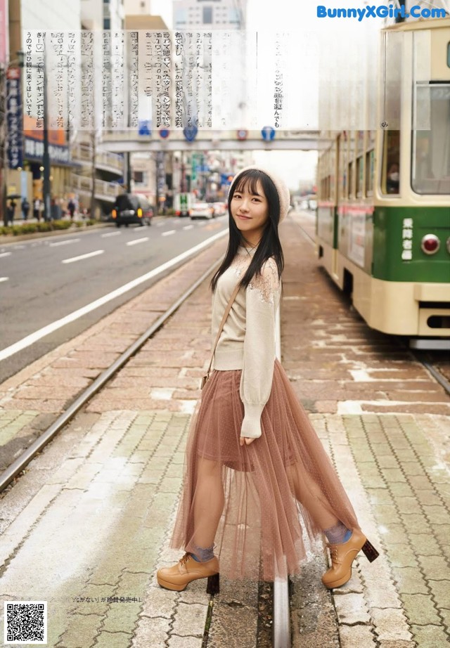 A woman standing on a train track in front of a tram.