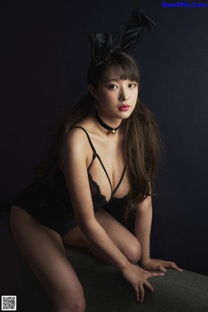 A woman in a black bodysuit sitting on a couch.