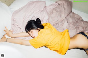 A woman in a yellow shirt and blue panties sitting on a bed.