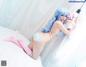 A woman in a white shirt and blue wig sitting on a bed.