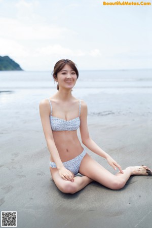 A woman in a blue and white bikini standing on a beach.
