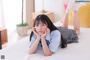 A woman in a blue shirt and gray skirt sitting on a couch.