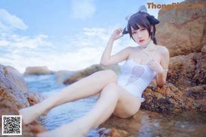 A woman in a white bathing suit sitting on a rock by the ocean.