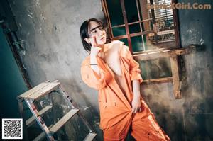 A woman in an orange jumpsuit holding a cell phone.