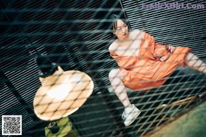 A woman in an orange jumpsuit working on a machine.